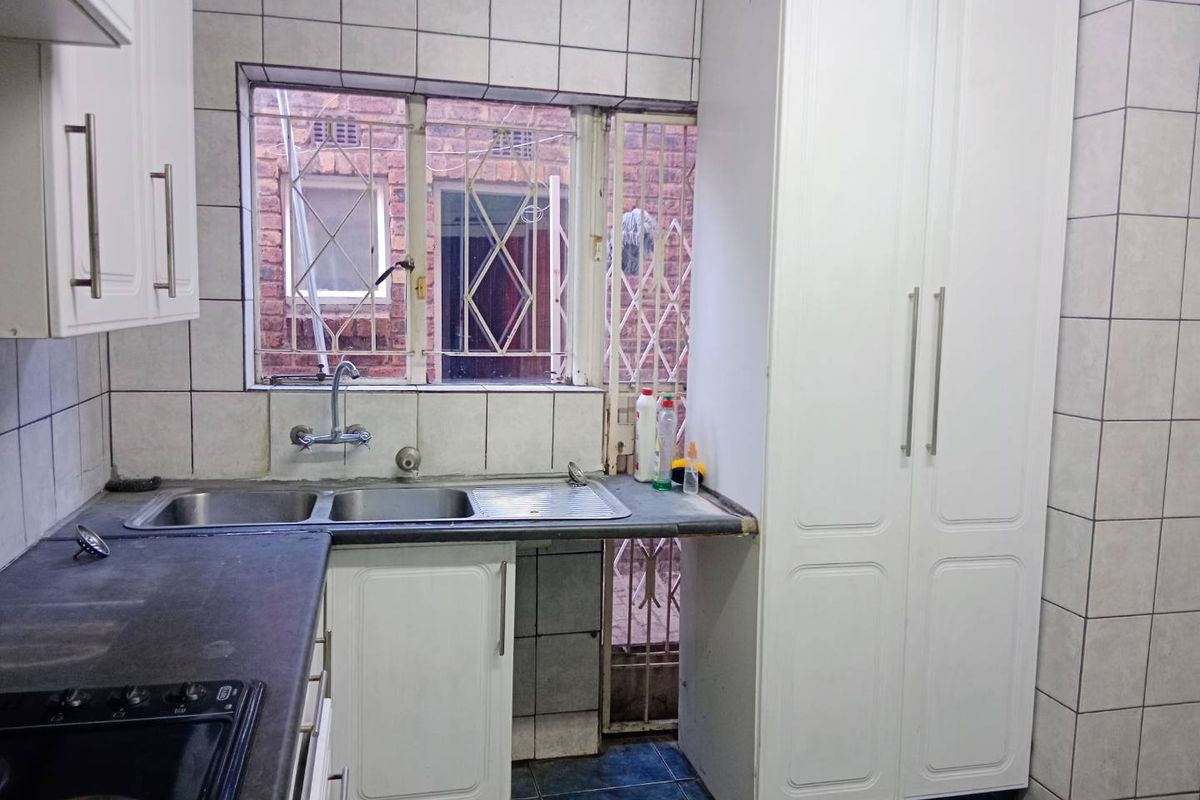 Functional kitchen featuring built-in cabinetry, double sink, tiled splashbacks, and a built-in hob, with direct access to an exterior security gate.