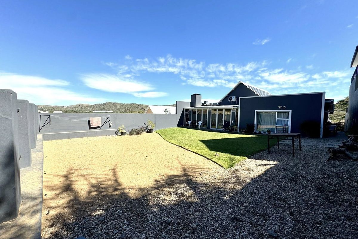 Rear view of the property featuring a landscaped garden with a lawn, gravel area, boundary wall, and access to the home via sliding glass doors.