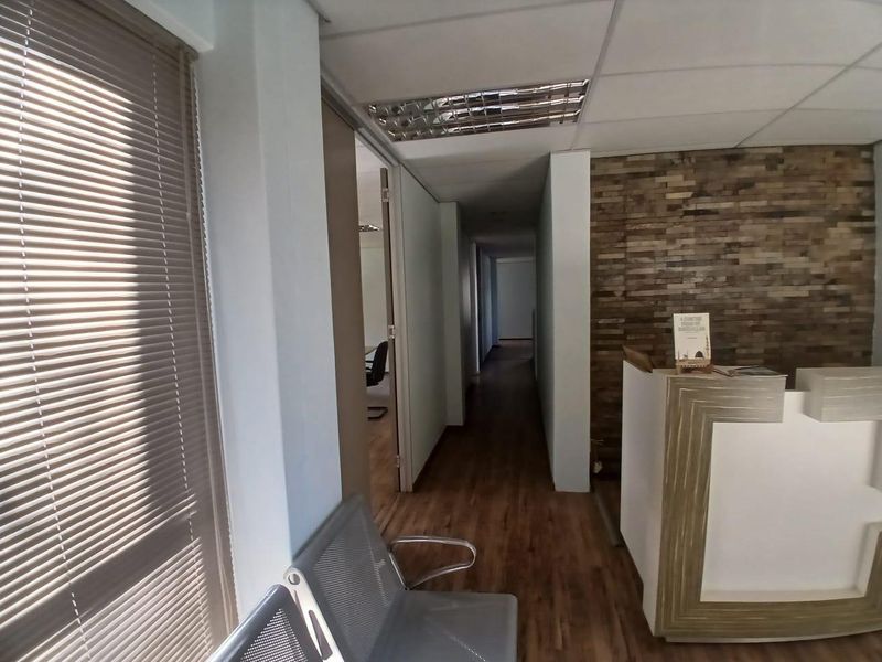 A professional office reception area featuring a stone veneer accent wall, laminate flooring, and a built-in reception desk leading into a central hallway.