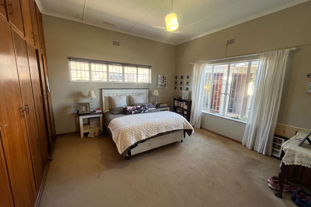 Spacious bedroom featuring built-in wooden cabinetry, large windows with security bars, and neutral wall finishes.