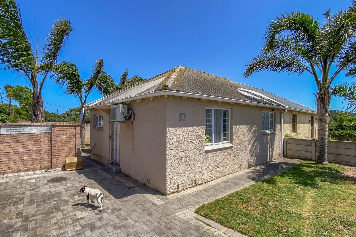 Rear exterior view of a single-story house featuring a paved driveway, boundary wall, and established palm trees under a clear blue sky.