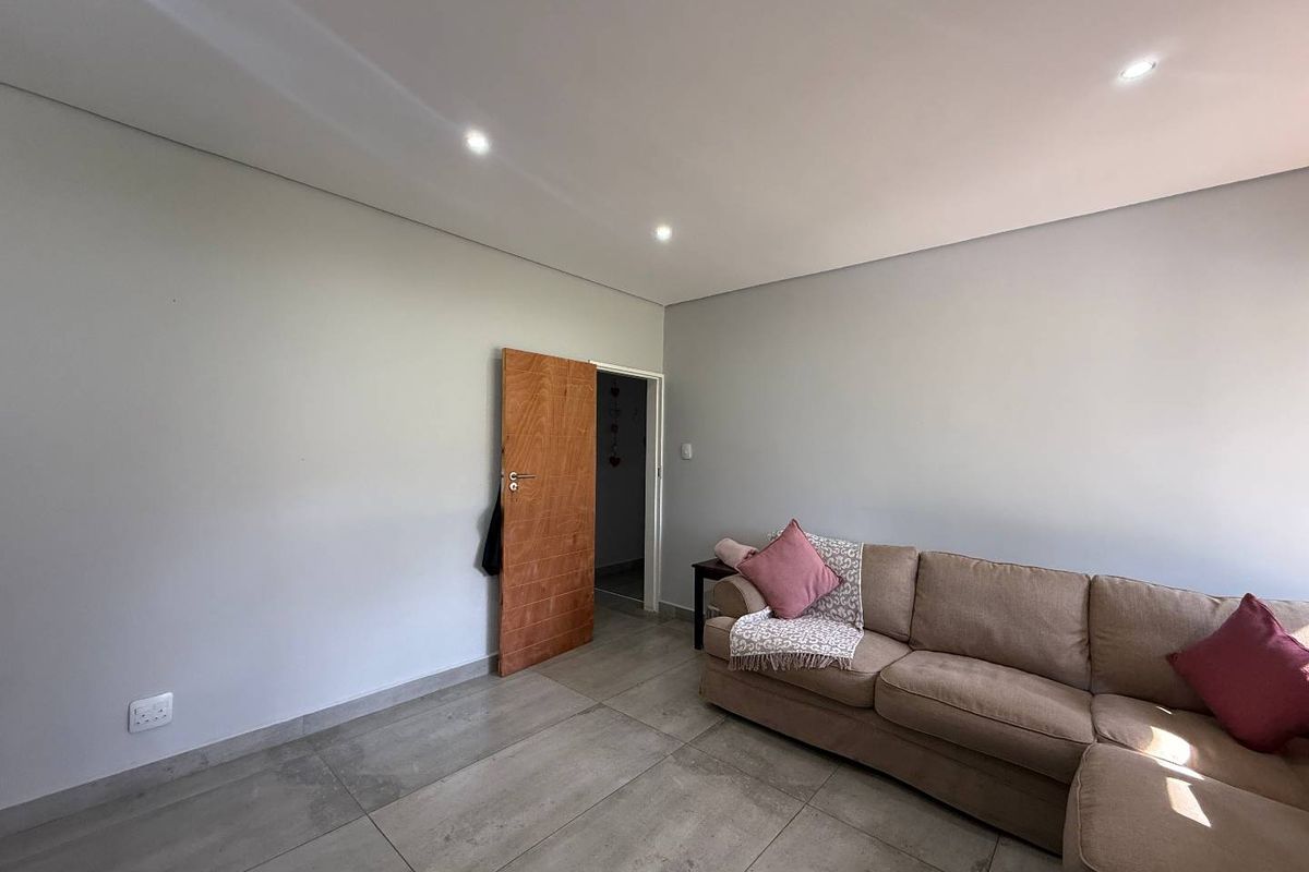 A bright living room featuring large format floor tiles, recessed downlighting, and a solid timber door leading to an adjacent space.