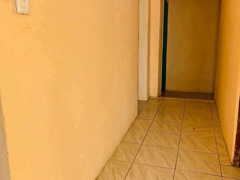 A vacant interior hallway featuring tiled flooring and plain peach-toned walls, providing access to adjacent rooms.