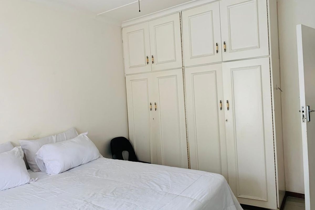 A bedroom featuring white built-in cupboards with overhead storage and a ceiling fan.