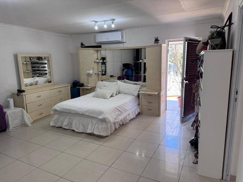 Spacious bedroom featuring tiled flooring, a split-system air conditioner, and a built-in headboard unit with integrated storage and mirrored panels.