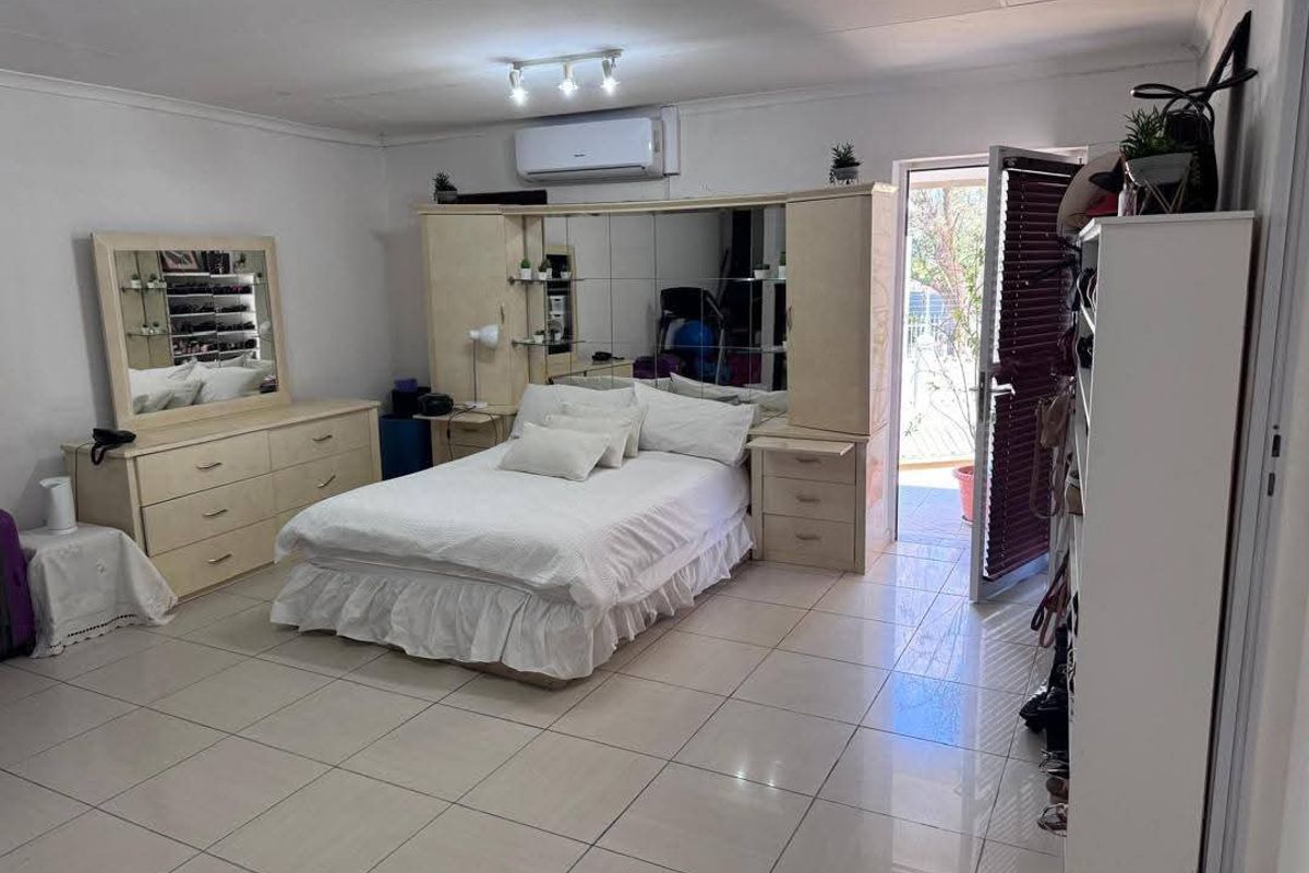 Spacious bedroom featuring tiled flooring, a split-system air conditioner, and a built-in headboard unit with integrated storage and mirrored panels.