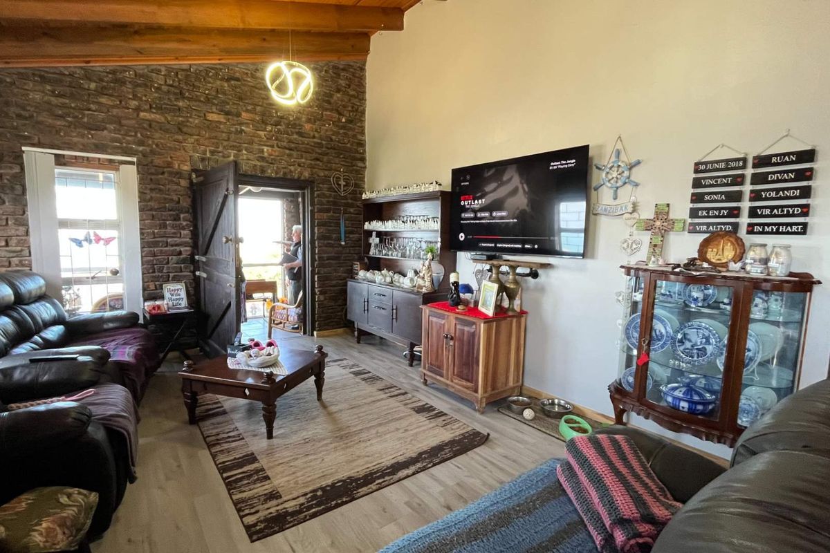 Spacious living room featuring a rustic exposed brick feature wall, high vaulted timber ceiling, and modern laminate flooring.