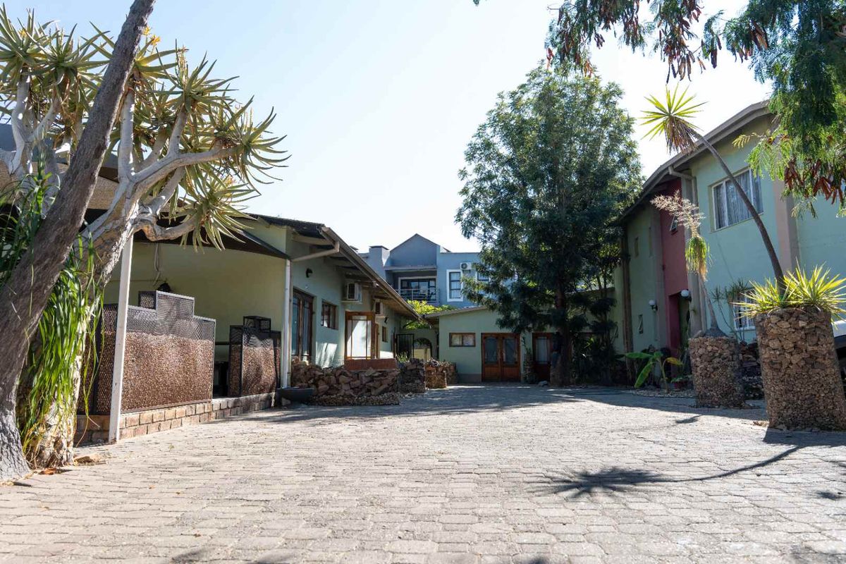 A paved courtyard area between hotel buildings featuring stone-clad pillars, a covered patio space, and mature landscaping.