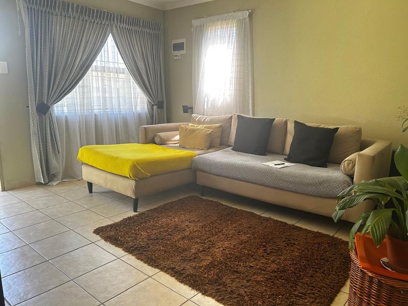 A comfortable living room featuring tiled flooring and large windows with installed curtain tracks, providing a bright and functional space.