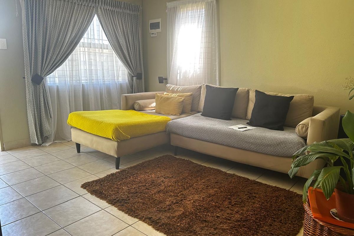 A comfortable living room featuring tiled flooring and large windows with installed curtain tracks, providing a bright and functional space.