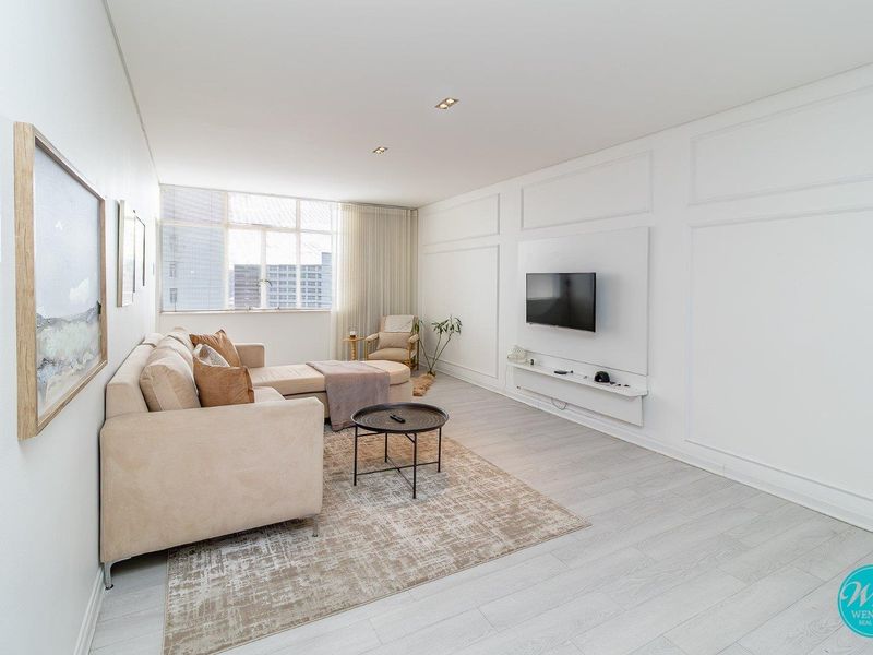A bright and modern living room featuring elegant wall paneling, recessed downlighting, and a sleek floating media console.