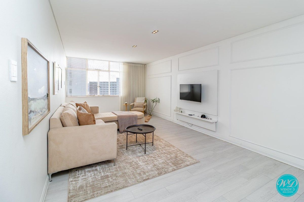 A bright and modern living room featuring elegant wall paneling, recessed downlighting, and a sleek floating media console.