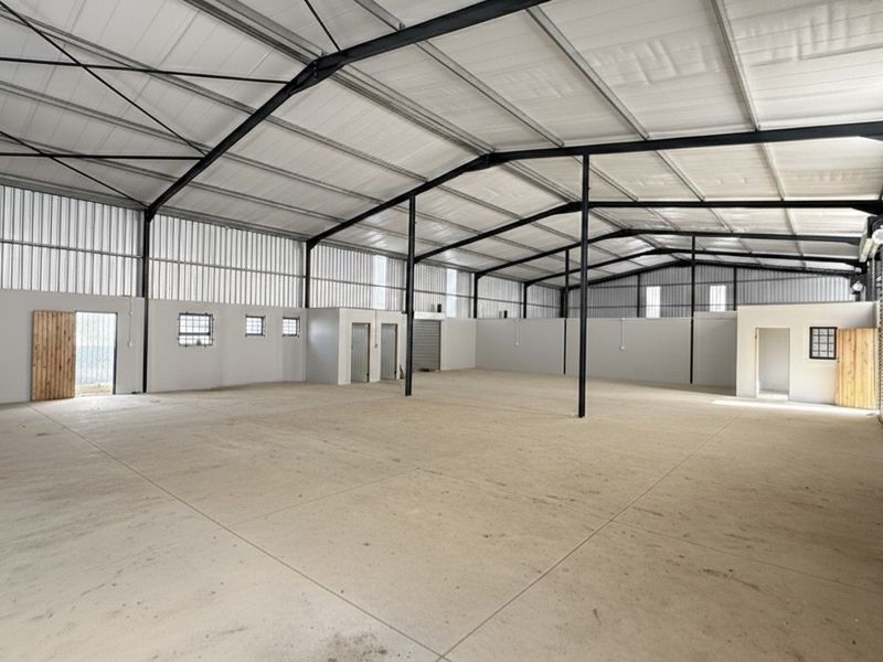 Spacious industrial warehouse featuring a high-clearance steel portal frame, concrete flooring, and large roller shutter access, suitable for various commercial or storage operations.