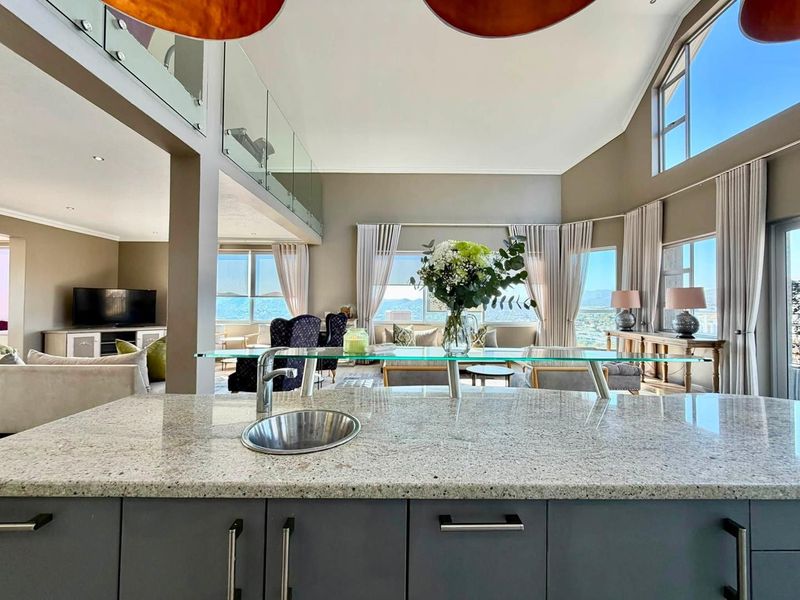 Spacious open-plan living area featuring a modern kitchen island with granite countertops, glass breakfast bar, and high vaulted ceilings with expansive views.