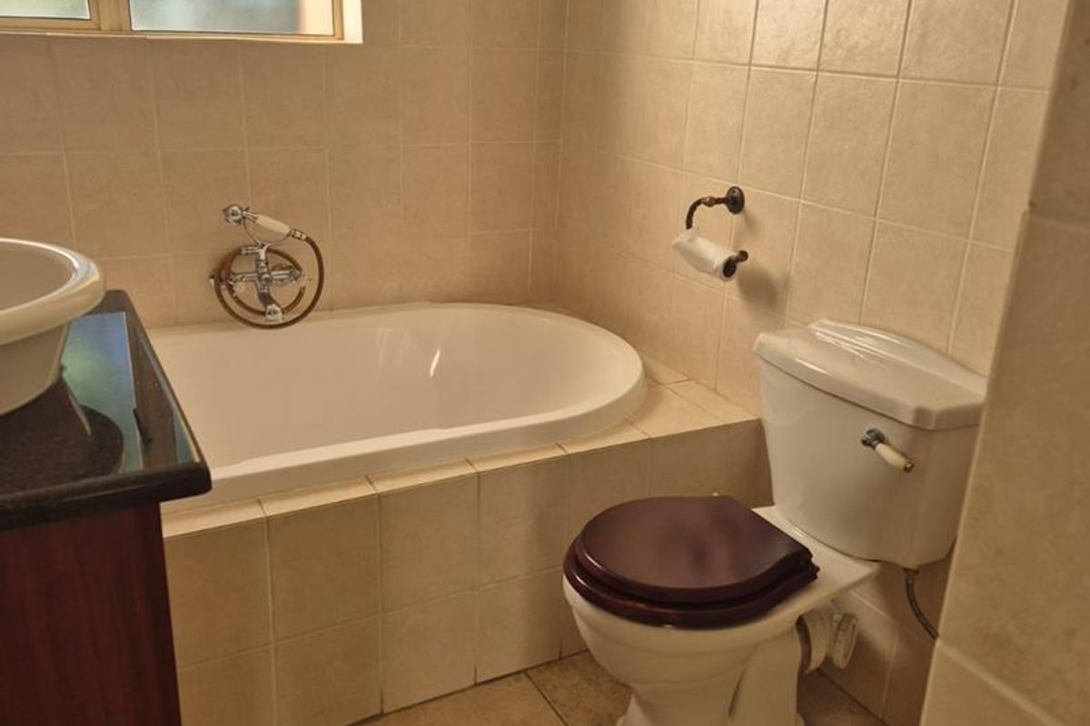 A functional bathroom featuring a built-in bathtub, tiled walls, a vanity with a basin, and a standard toilet.
