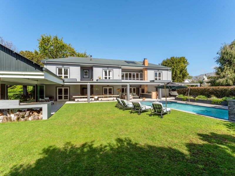 Spacious rear exterior featuring a well-maintained lawn, swimming pool, and a large covered patio with a built-in braai area.