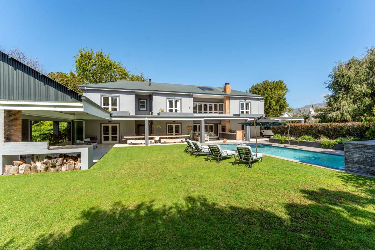 Spacious rear exterior featuring a well-maintained lawn, swimming pool, and a large covered patio with a built-in braai area.
