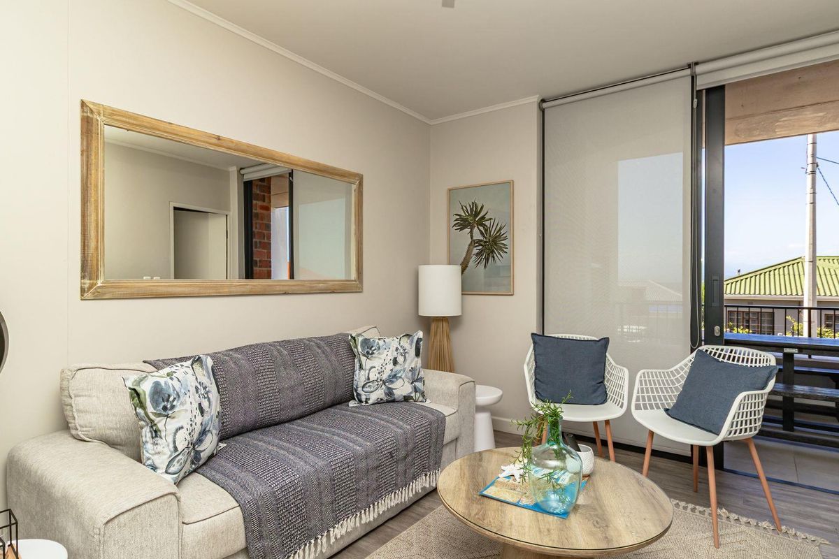 A bright living room featuring neutral walls, wood-look flooring, and large sliding glass doors that open onto a private balcony.