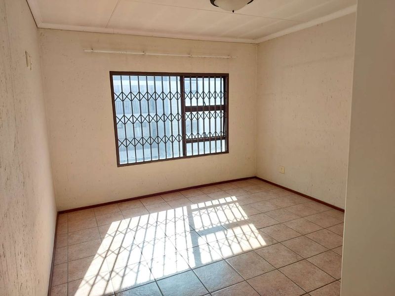 An empty bedroom featuring tiled flooring and security bars on the window, requiring cosmetic updates to the wall finishes.