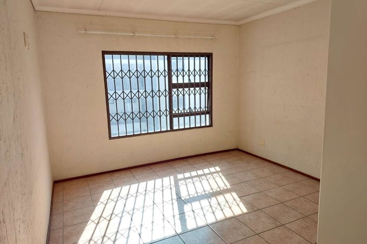 An empty bedroom featuring tiled flooring and security bars on the window, requiring cosmetic updates to the wall finishes.