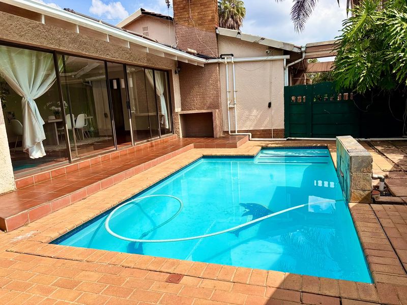 Outdoor pool area featuring a swimming pool, brick paving, and a covered patio with sliding door access to the main living space.