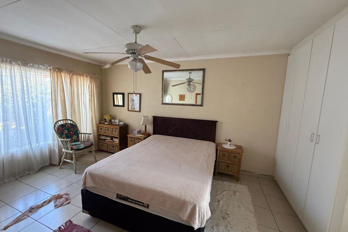 A well-lit bedroom featuring neutral tiled flooring, a ceiling fan, and ample built-in cupboard storage space.