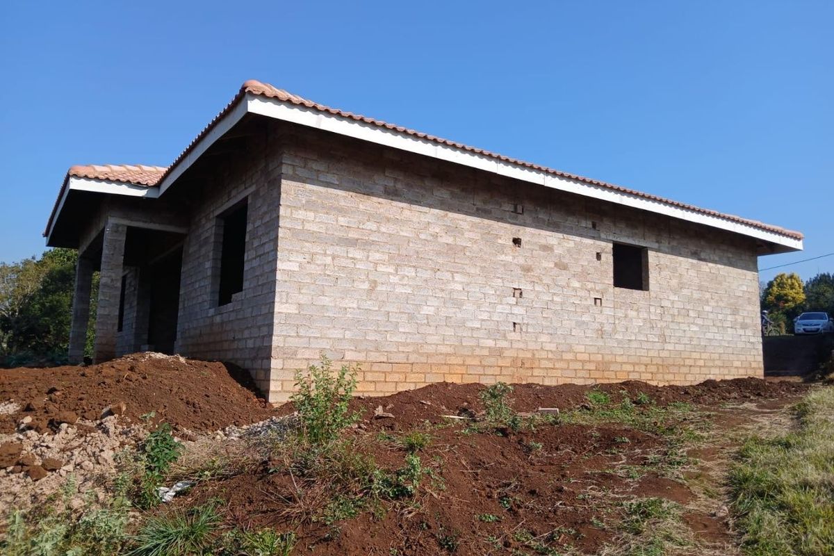 A rear view of a house under construction featuring exposed concrete block masonry walls and a completed tiled roof structure.