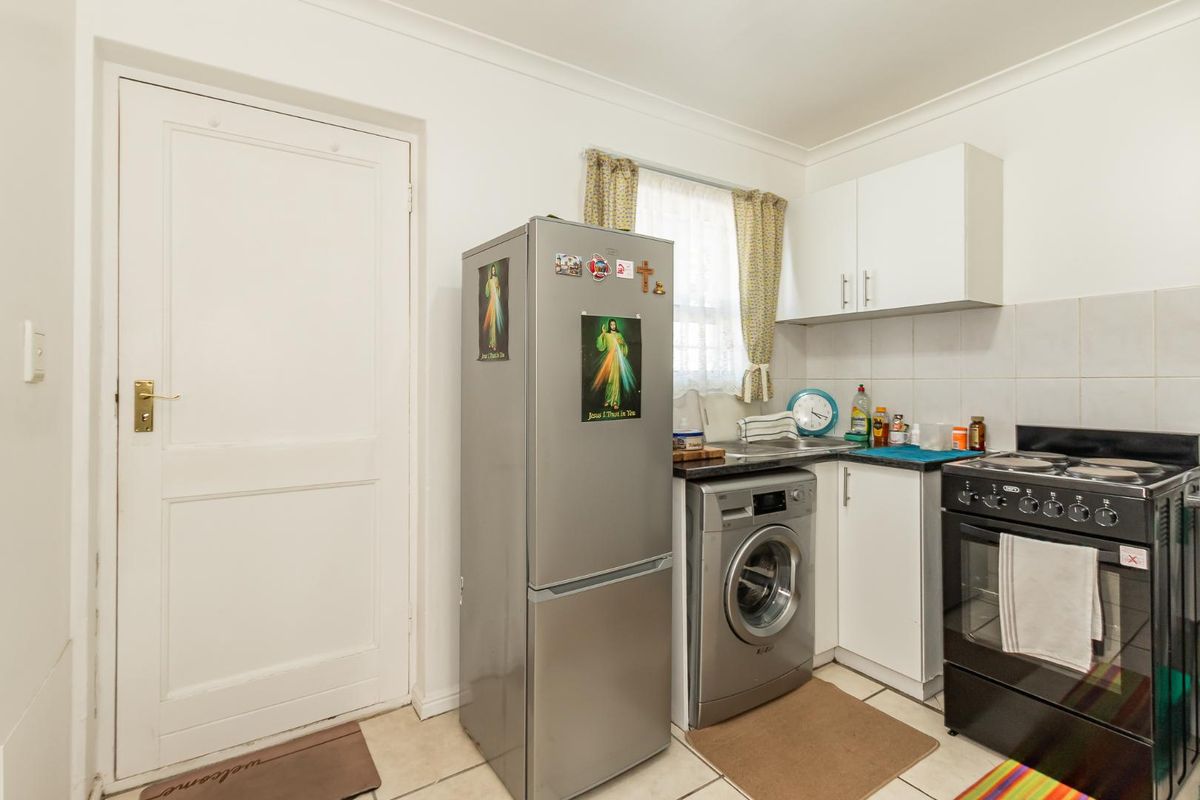 Compact kitchen area featuring tiled flooring, white cabinetry, and space for a washing machine and freestanding stove.