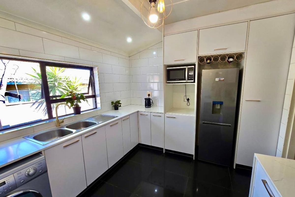 Modern kitchen featuring white cabinetry, subway tile backsplash, double stainless steel sink, and integrated appliance housing with dark tiled flooring.