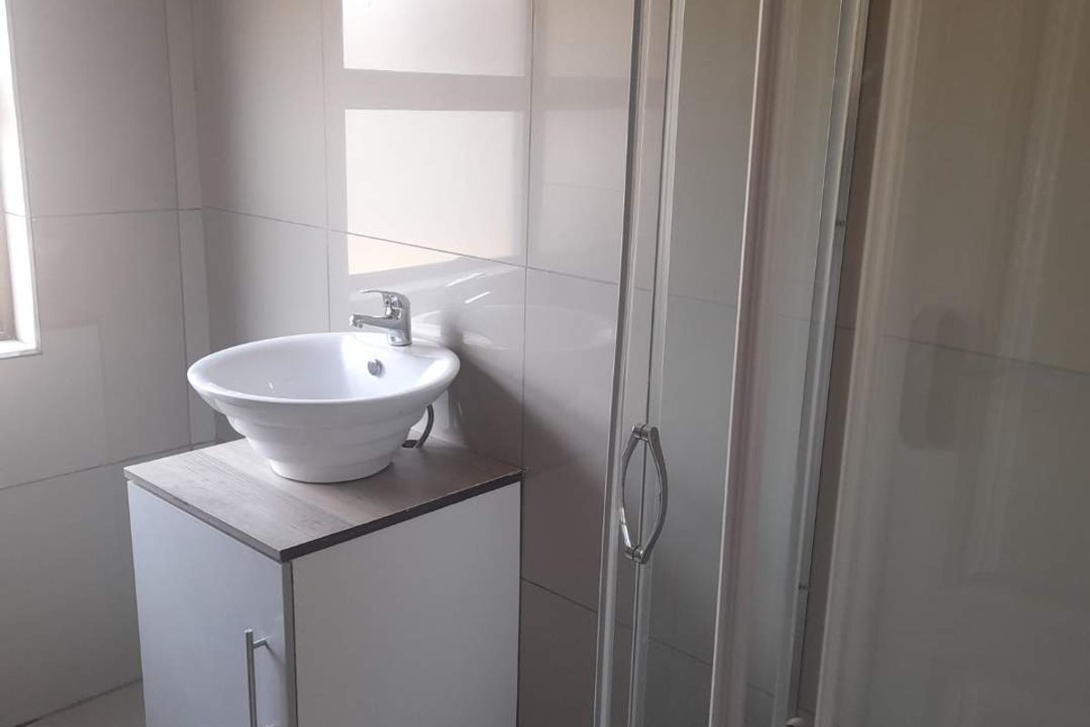 A modern bathroom featuring a white vessel sink on a vanity cabinet and a glass-enclosed shower stall with neutral wall tiling.
