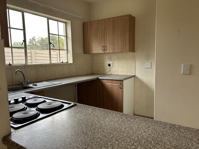 A functional kitchen featuring laminate cabinetry, a granite-look countertop, an integrated electric hob, and a stainless steel sink with a tiled splashback.