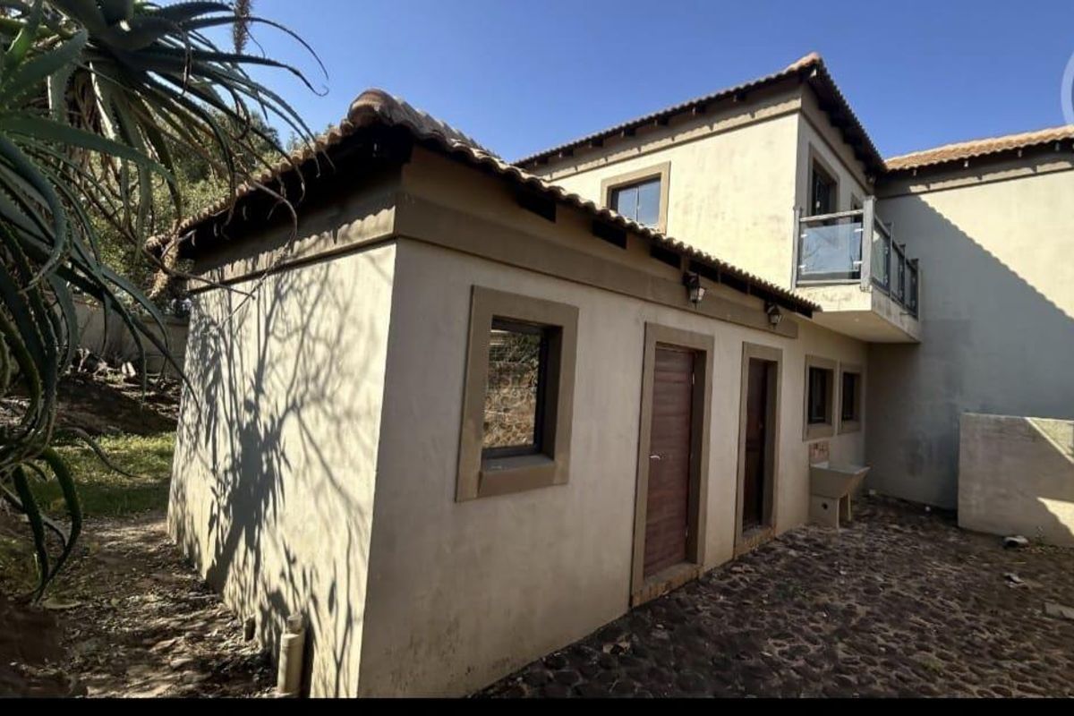 Rear exterior view of the property featuring a paved courtyard, external utility sink, and an upper-level balcony with glass balustrade.
