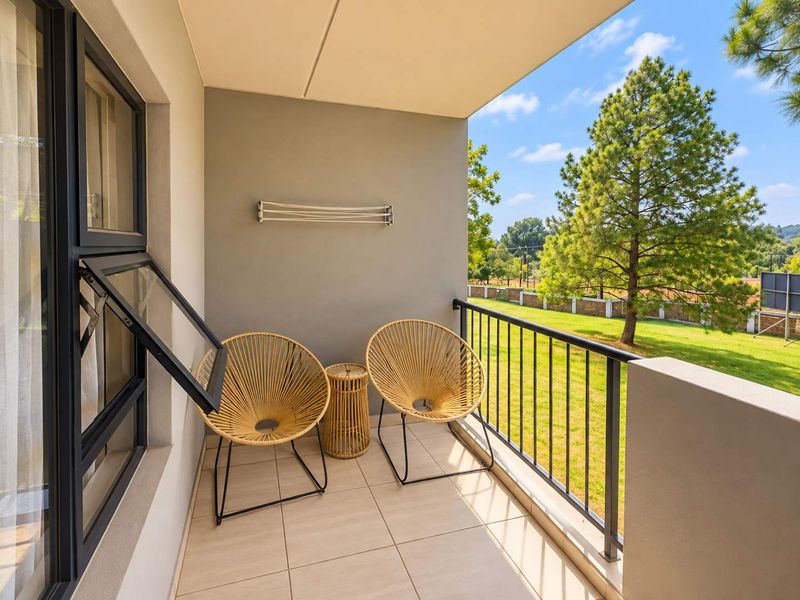 A well-maintained covered balcony featuring tiled flooring, a metal balustrade, and a wall-mounted drying rack, overlooking a green garden area.
