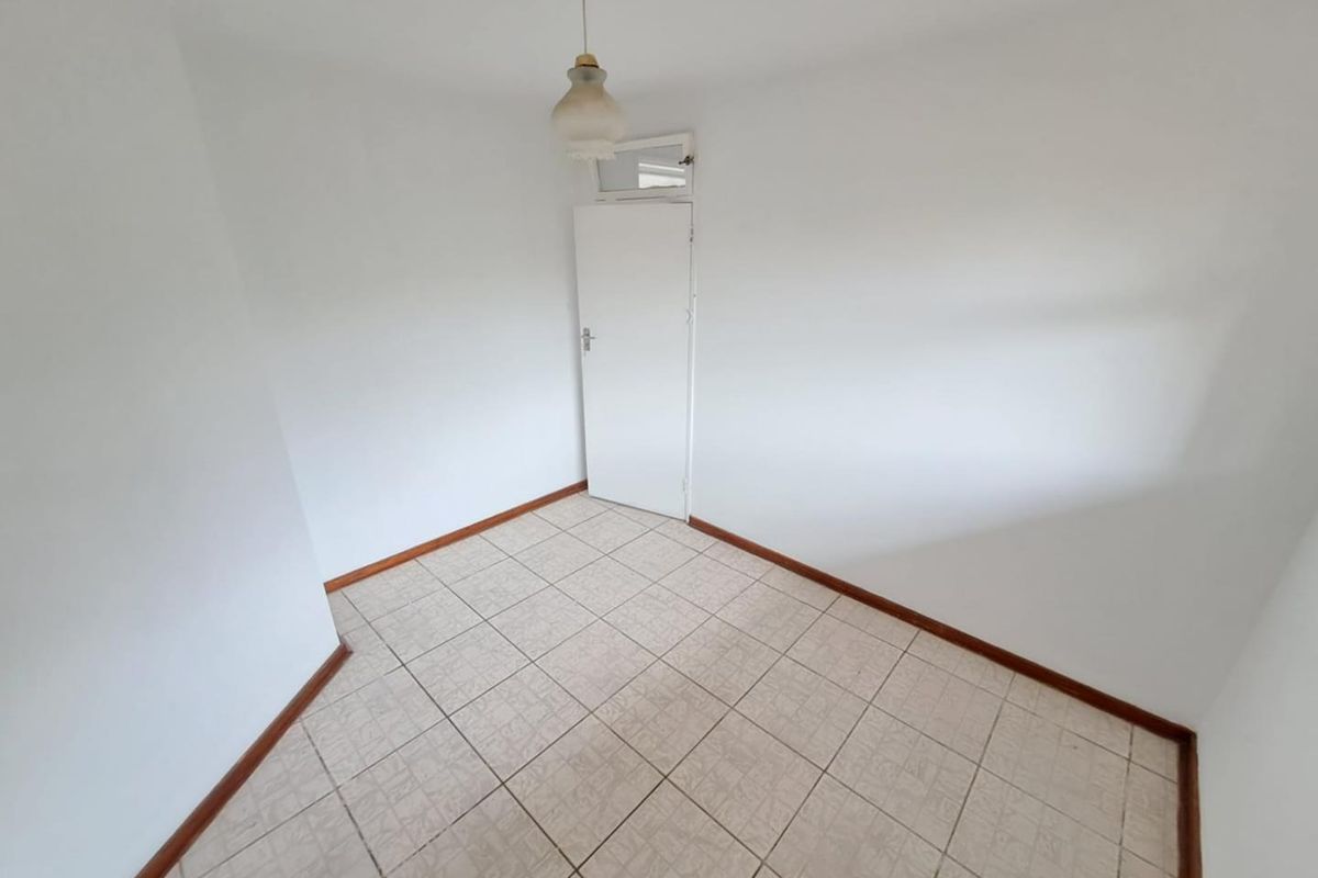 A vacant, neutrally painted bedroom featuring tiled flooring and a simple pendant light fixture.