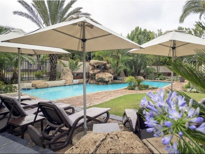 A well-maintained outdoor pool area featuring a natural rock water feature, paved decking, and established garden landscaping.