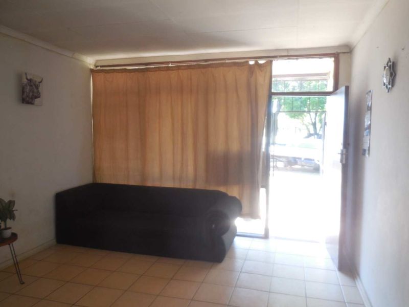 A living room area featuring tiled flooring, a large window with curtains, and direct access to the exterior.