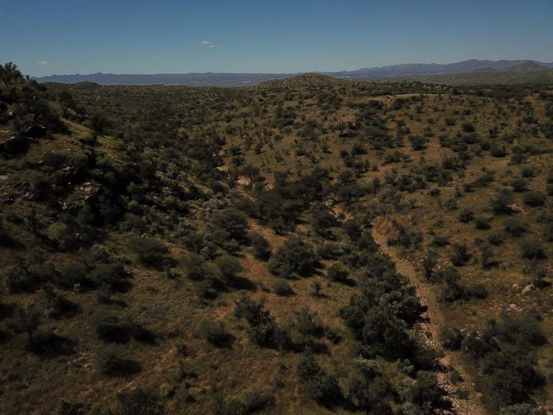An aerial view of the expansive, natural landscape featuring native vegetation and rocky terrain, showcasing the property's vast and scenic surroundings.