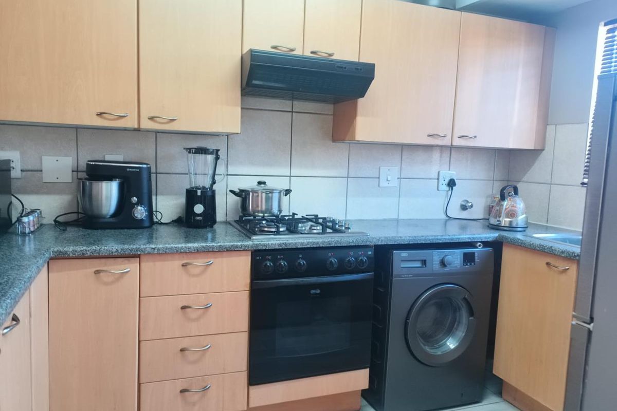 A functional kitchen featuring light wood-finish cabinetry, granite countertops, a gas hob with extractor fan, and a built-in oven with an integrated washing machine.