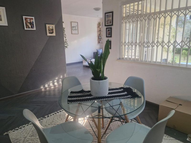A bright dining area featuring a textured accent wall, herringbone flooring, and a window fitted with a security gate.