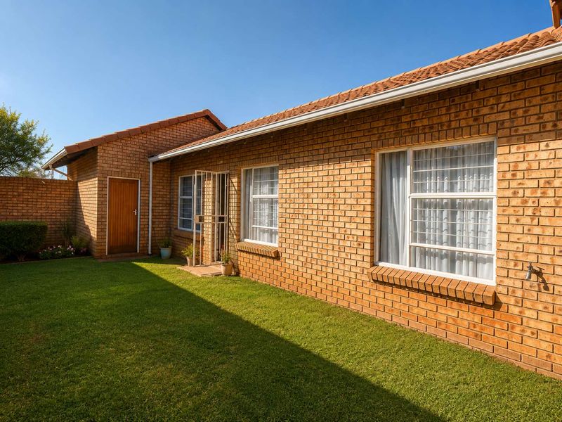 A well-maintained rear exterior view of the townhouse featuring face brick walls, a tiled roof, and a neat private lawn area.