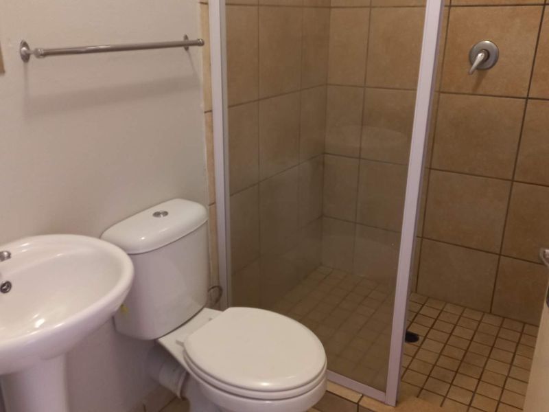 A functional bathroom featuring a pedestal basin, toilet, and a tiled shower enclosure with a glass door.