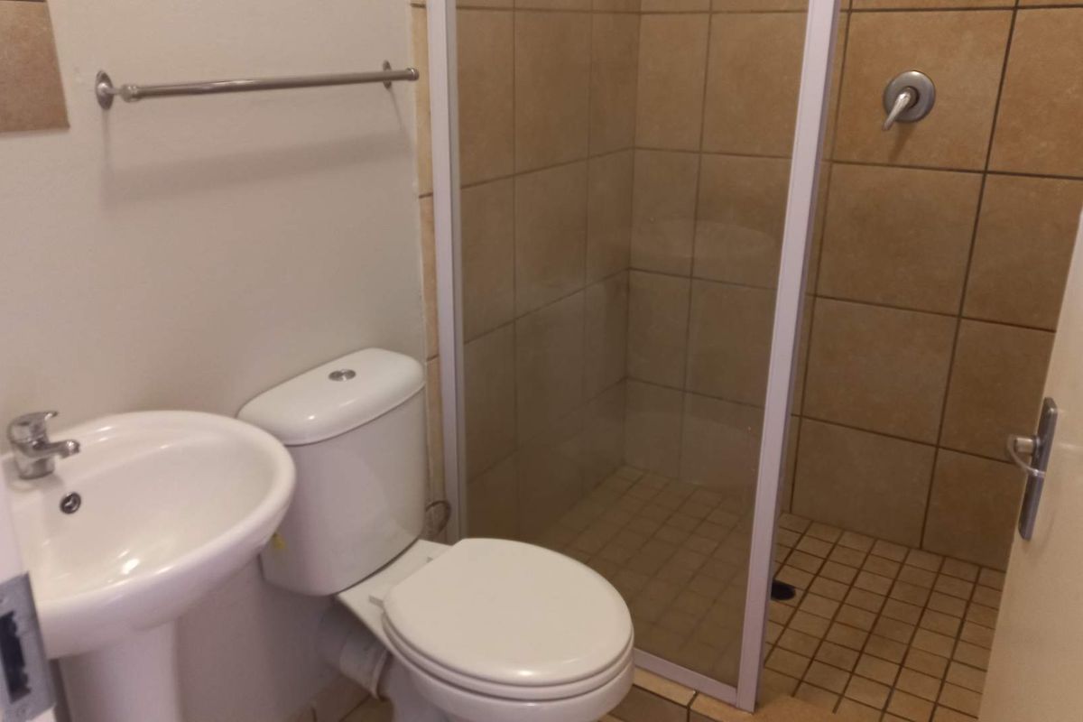A functional bathroom featuring a pedestal basin, toilet, and a tiled shower enclosure with a glass door.