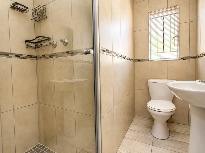 A clean, functional bathroom featuring a glass-enclosed shower, pedestal basin, and toilet with neutral wall and floor tiling.
