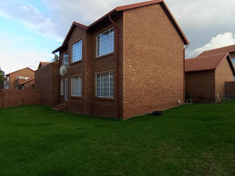 Rear view of a two-story face brick apartment building featuring a private lawn area and secure window bars.