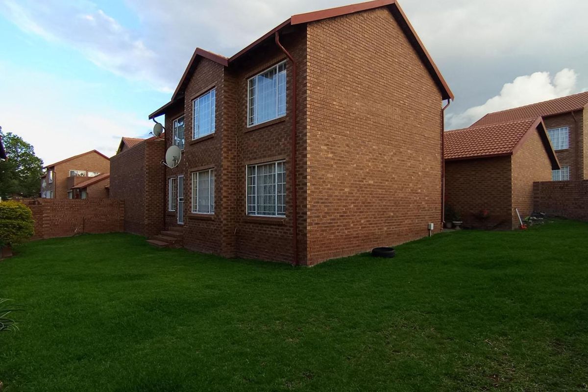 Rear view of a two-story face brick apartment building featuring a private lawn area and secure window bars.