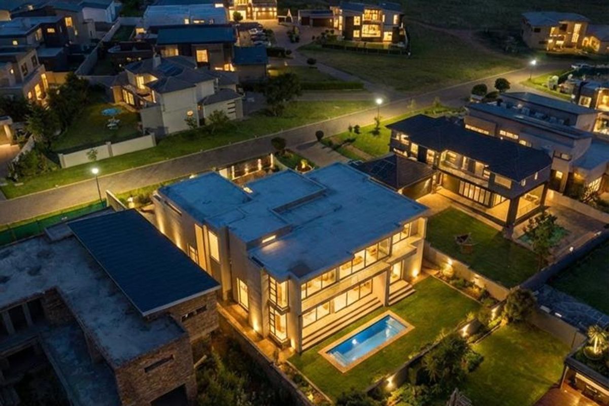 Aerial night view of a modern residential property featuring a swimming pool, landscaped garden, and contemporary architectural design within a suburban estate.