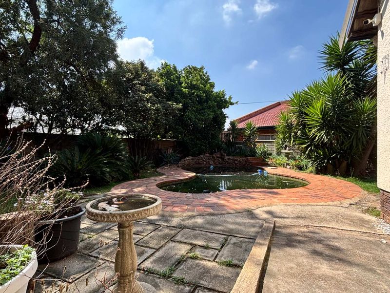Outdoor pool area featuring a kidney-shaped pool with brick surround, concrete patio space, and established garden landscaping.
