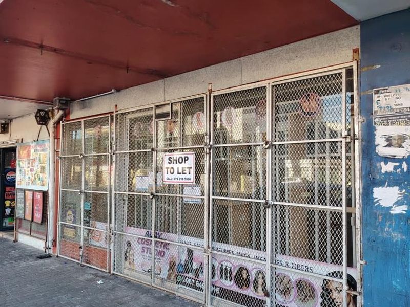 Street-level commercial storefront featuring a secure metal gate, paved walkway, and overhead awning, currently available for lease.