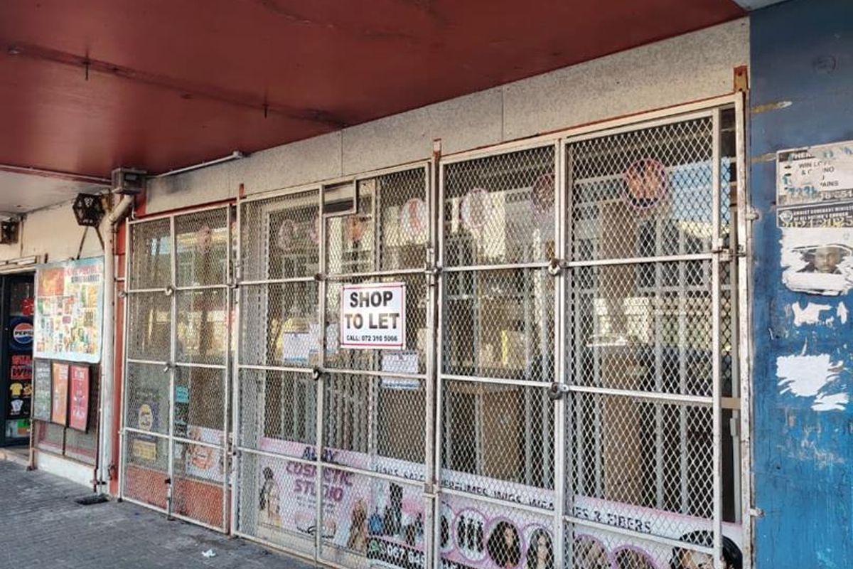 Street-level commercial storefront featuring a secure metal gate, paved walkway, and overhead awning, currently available for lease.