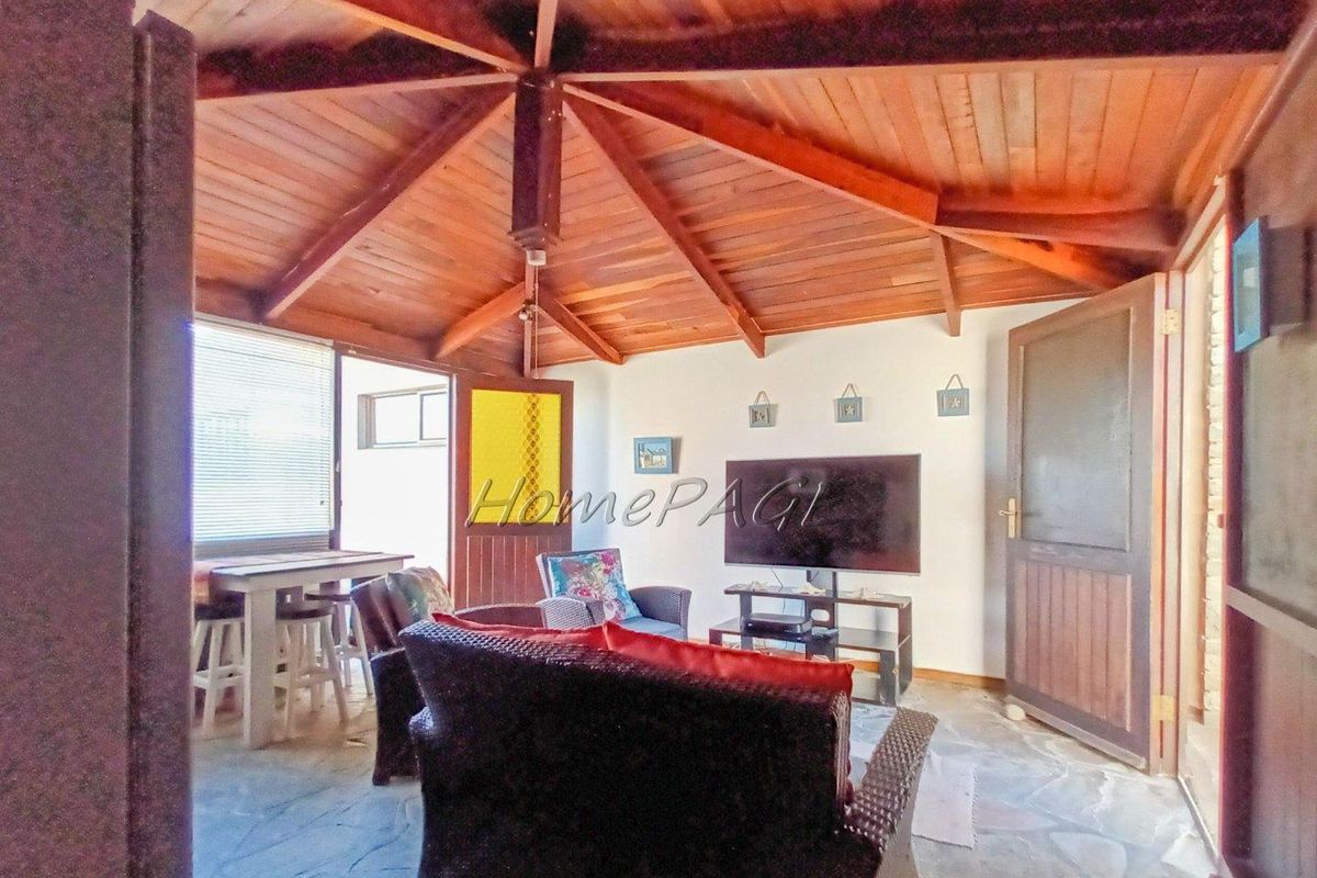 A cozy living area featuring a vaulted timber ceiling, stone flooring, and direct access to outdoor spaces through multiple doors.